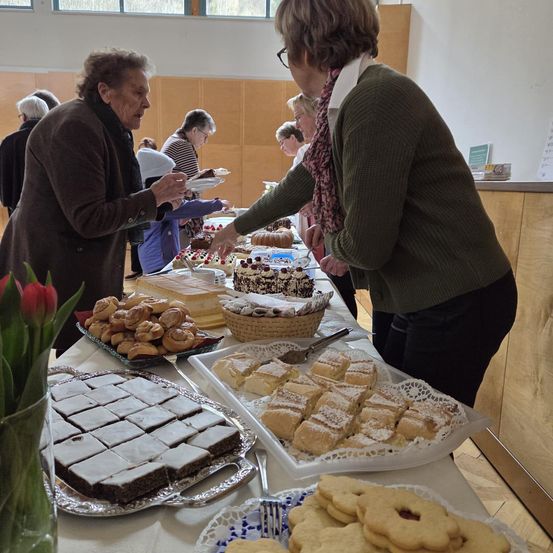 Mehrere ältere Frauen wählen Desserts von einem Buffet aus. Eine Vielzahl von Gebäck und Kuchen ist auf Tabletts und Tellern ausgestellt.