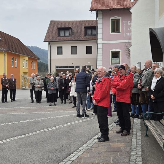 Eine Gruppe von Menschen, einige in Uniformen, stehen vor einem Gebäude. Sie scheinen auf ein Ereignis zu warten.
