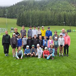 Eine Gruppe von Kindern und Erwachsenen posiert für ein Foto auf einem Rasenfeld mit Bergen im Hintergrund.