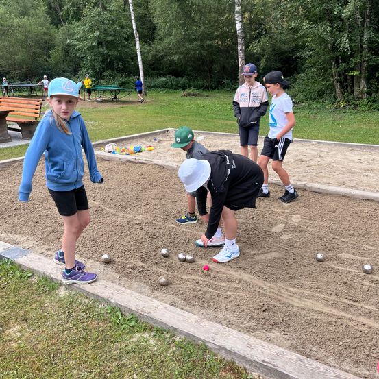 Kinder spielen Boccia auf einem sandigen Platz, ein Kind beugt sich vor, um einen Ball aufzuheben.