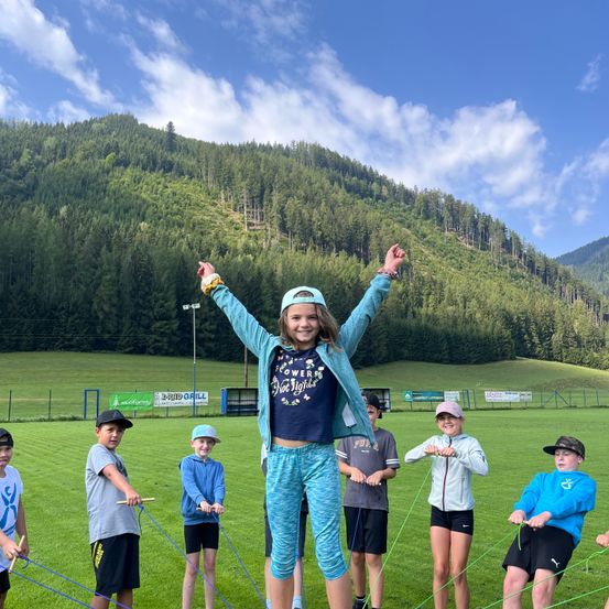 Eine Gruppe von Kindern macht Jumping Jacks auf einem Rasenfeld mit einem Berg im Hintergrund.