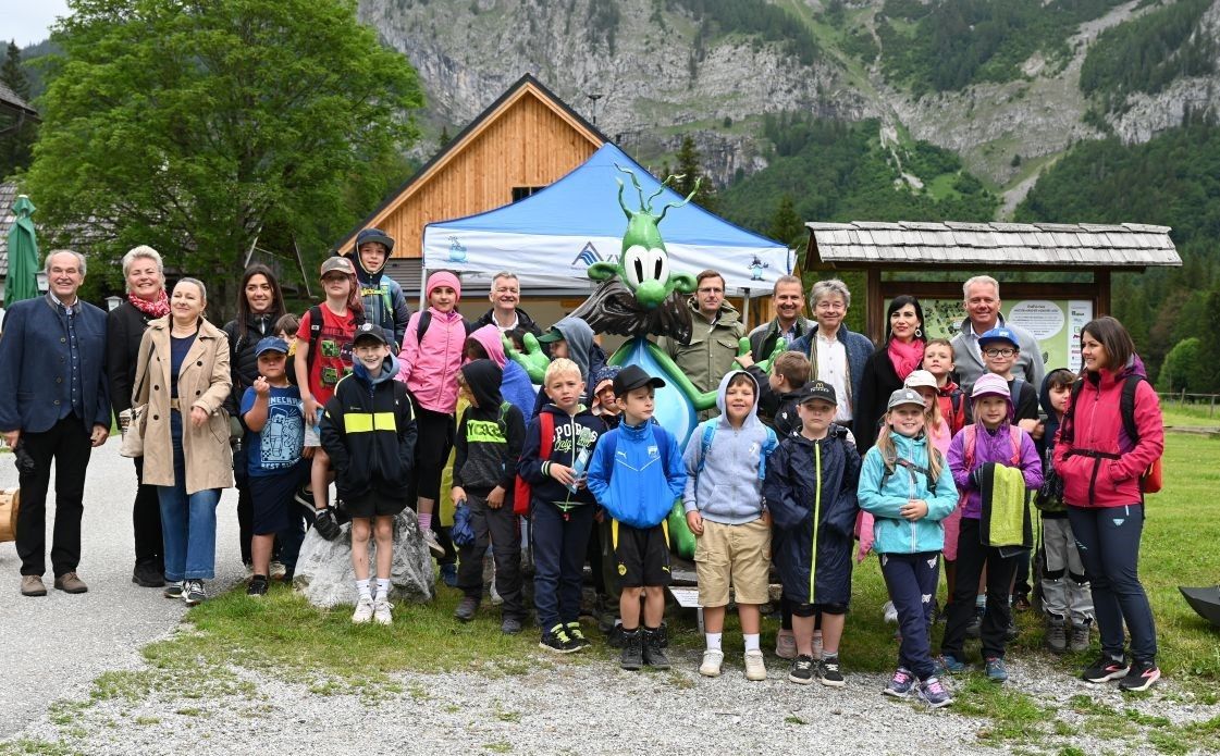 Eine Gruppe von Kindern und Erwachsenen posiert für ein Foto vor einer Bergkulisse, mit einem großen grünen Ballon und einem Zelt im Hintergrund.