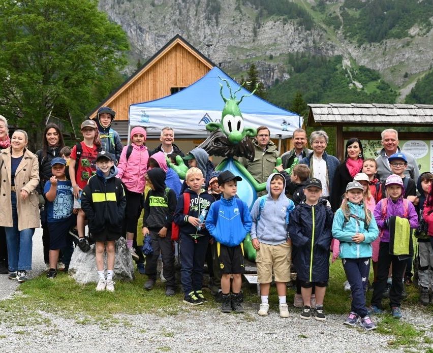 Eine Gruppe von Kindern und Erwachsenen posiert für ein Foto vor einer Bergkulisse, mit einem großen grünen Ballon und einem Zelt im Hintergrund.