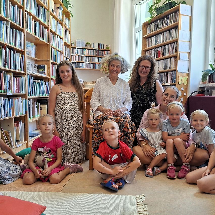 Eine Gruppe von Kindern und Erwachsenen sitzt und steht in einer Bibliothek, lächelt und posiert für ein Foto.