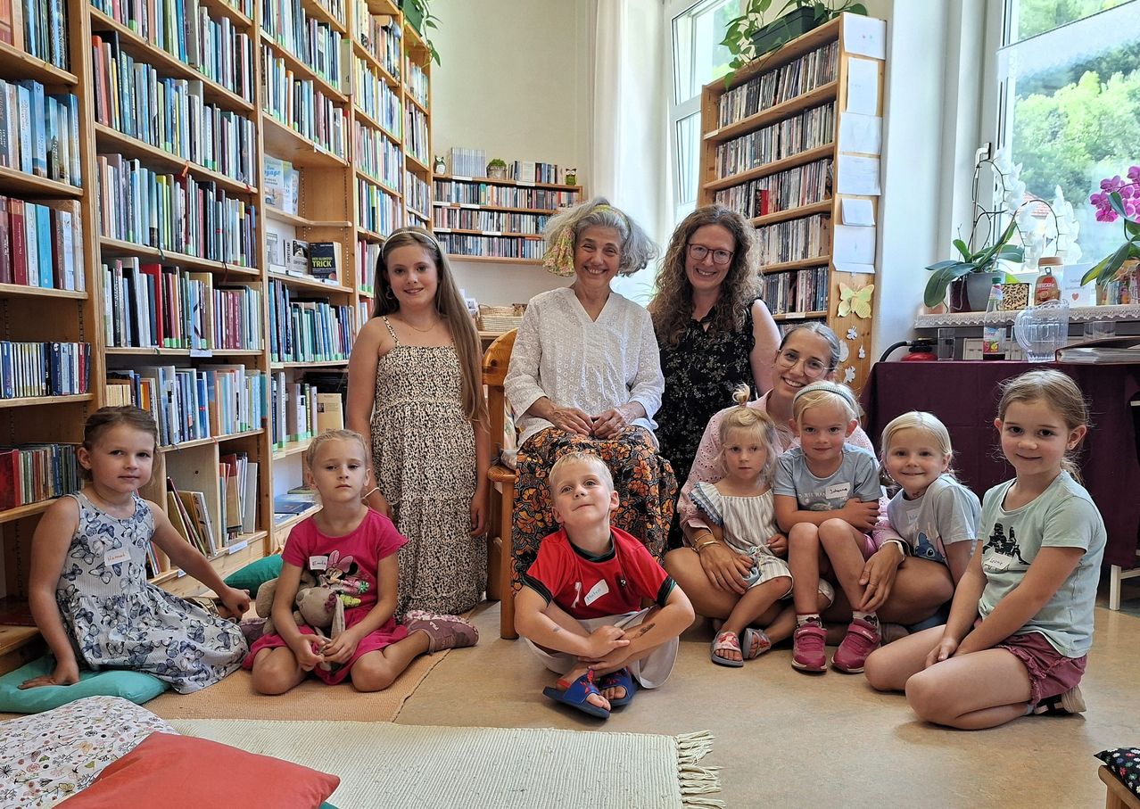 Eine Gruppe von Kindern und Erwachsenen sitzt und steht in einer Bibliothek, lächelt und posiert für ein Foto.