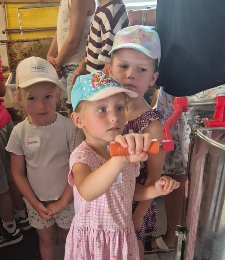 Three young girls in a room, one girl in pink is holding a tool and looking at a machine.