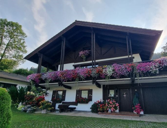 Ein reizendes Haus mit einem Balkon, der mit bunten Blumen geschmückt ist, einer Bank und einem Baum im Hintergrund.