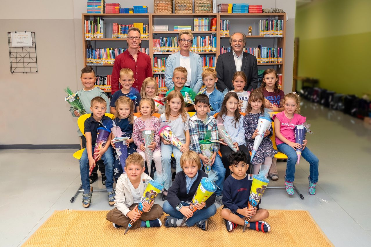 Eine Gruppe von Kindern und Erwachsenen in einer Bibliothek, die Kegel halten und für ein Foto lächeln.