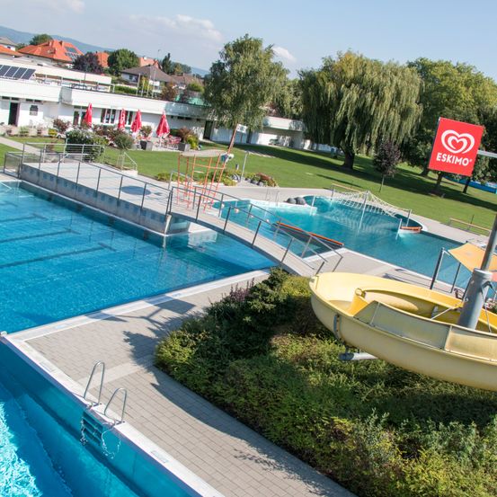 Ein Außenpool mit zwei Becken, einem großen und einem kleineren, mit einer gelben Wasserrutsche und einem roten Eskimo-Schild im Hintergrund.