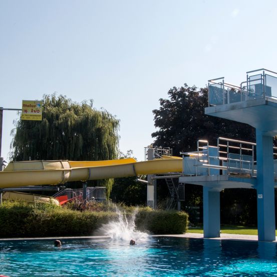 Eine gelbe Wasserrutsche an einem Freibad mit Schwimmern unter einer Sprungturm.