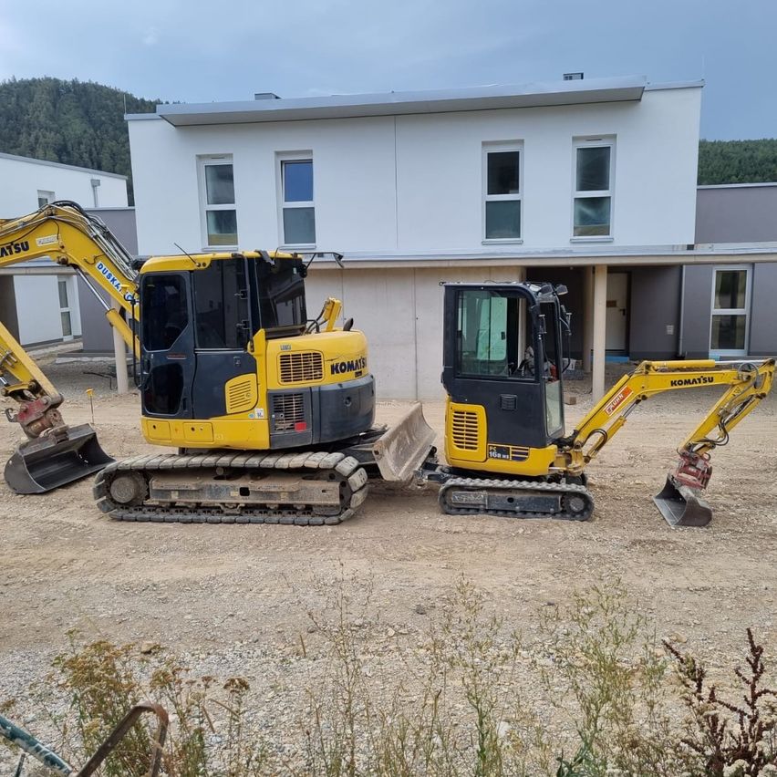 Zwei gelbe Komatsu-Bagger stehen auf einer Erdeinfahrt vor einem modernen Haus geparkt.