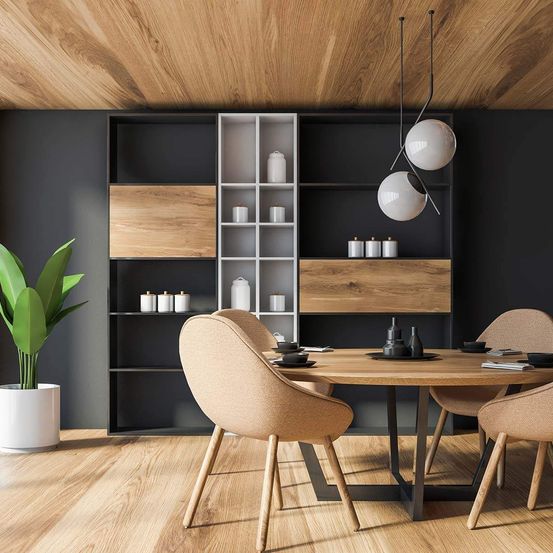Ein modernes Esszimmer mit Holzboden, einer Holzdecke und einer schwarzen Wand. Ein runder Tisch mit vier Stühlen, einem Regal mit Gläsern und einer Pflanze. Zwei hängende Lampen verleihen dem Raum einen dekorativen Touch.