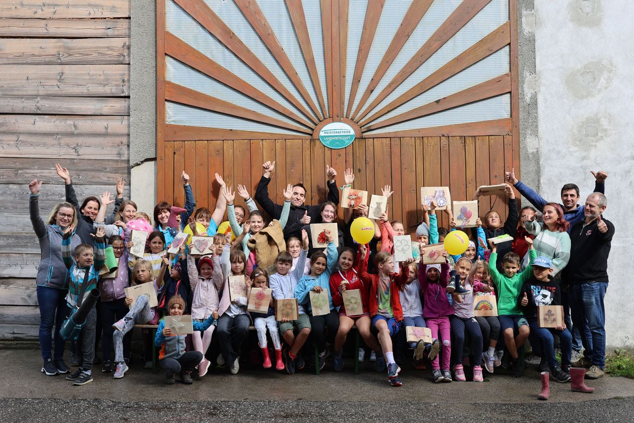 Eine Gruppe von Kindern und Erwachsenen posiert für ein Foto vor einem Gebäude. Sie alle haben Zeichnungen und einige haben Luftballons.