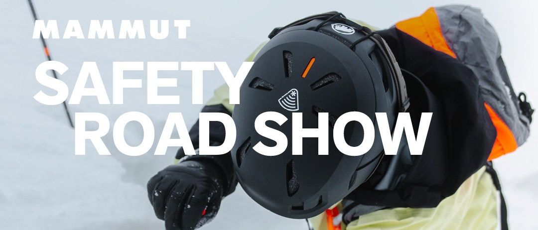Eine Person in Mammut-Markenkleidung schaufelt Schnee, während sie in einem Schneehaufen steht. Der Text lautet 'Mammut Safety Road Show'.
