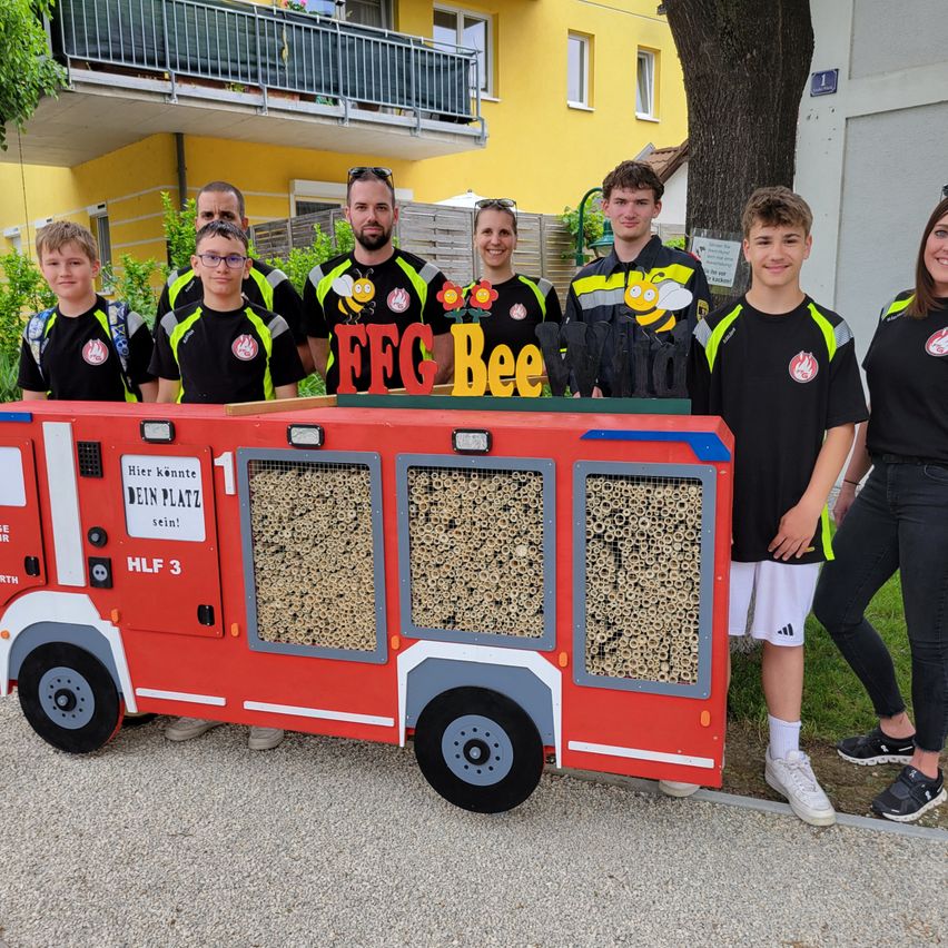Eine Gruppe von Menschen posiert vor einem roten Feuerwehrauto mit Bienenstöcken darauf.