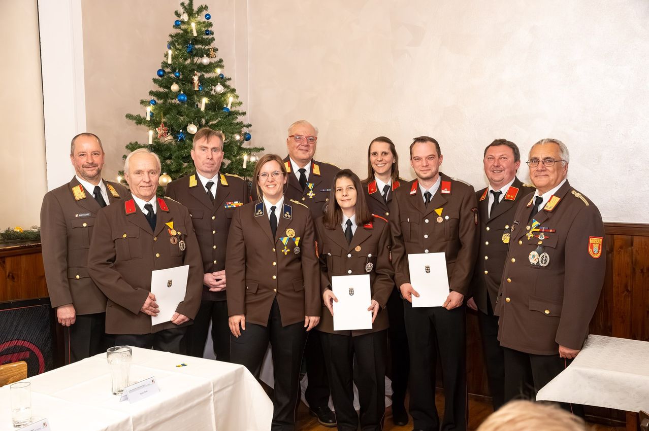 Eine Gruppe von Militärangehörigen steht in formellen Uniformen, Urkunden in der Hand, für ein Foto vor einem geschmückten Weihnachtsbaum.