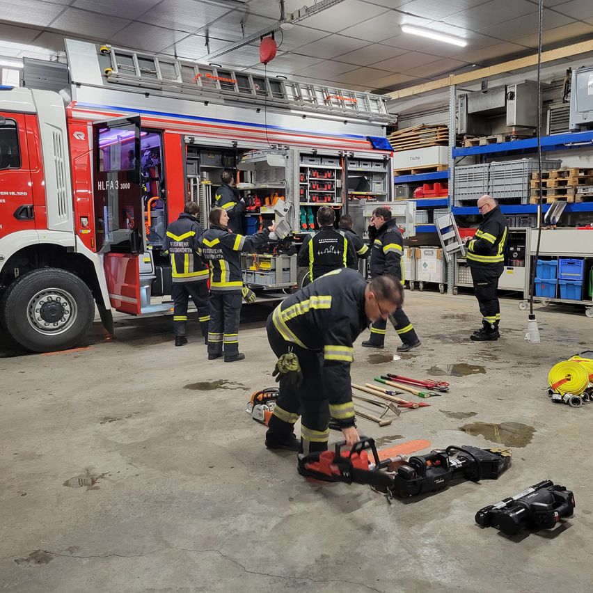 Feuerwehrleute überprüfen Ausrüstung in einem in einer Garage geparkten Feuerwehrwagen. Werkzeuge liegen verstreut auf dem Boden.
