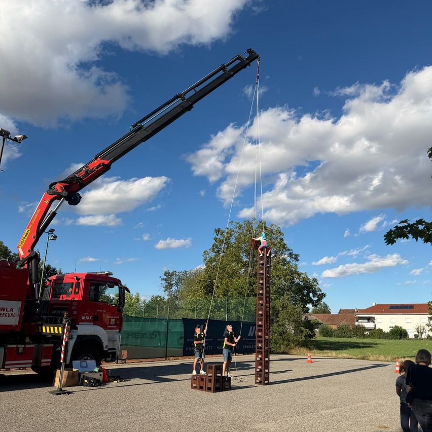 A fire truck with a crane is lifting two people up a vertical ladder in a park.
