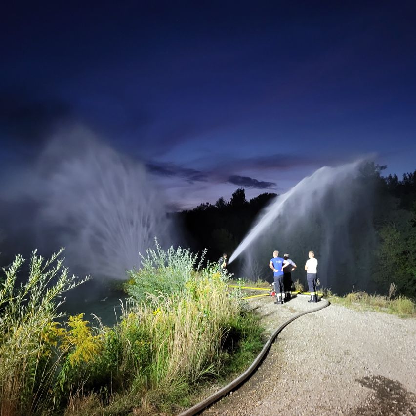 Firefighters are spraying water from a hose into a river at night.