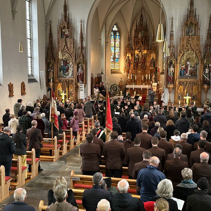 Eine Gemeinde in einer Kirche versammelt sich für einen Gottesdienst mit Chor und Blechbläserensemble. Der Altar ist mit religiöser Kunst geschmückt.