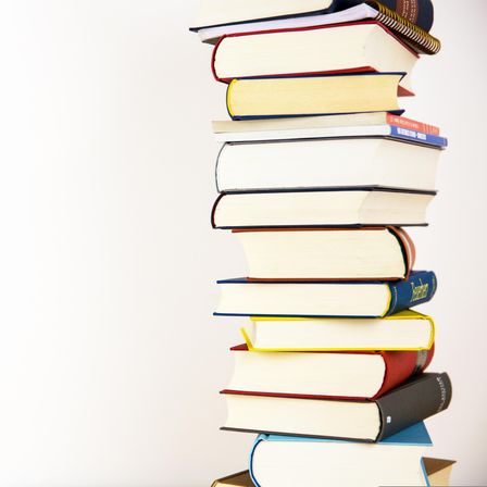 Ein Stapel Bücher mit weißen, blauen, roten und gelben Buchrücken wird vor einem weißen Hintergrund gezeigt.
