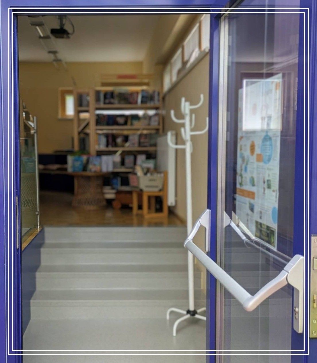 A view through an open blue door into a room with a bookshelf, a table, and a white coat rack. The room has a wooden floor and a white wall.