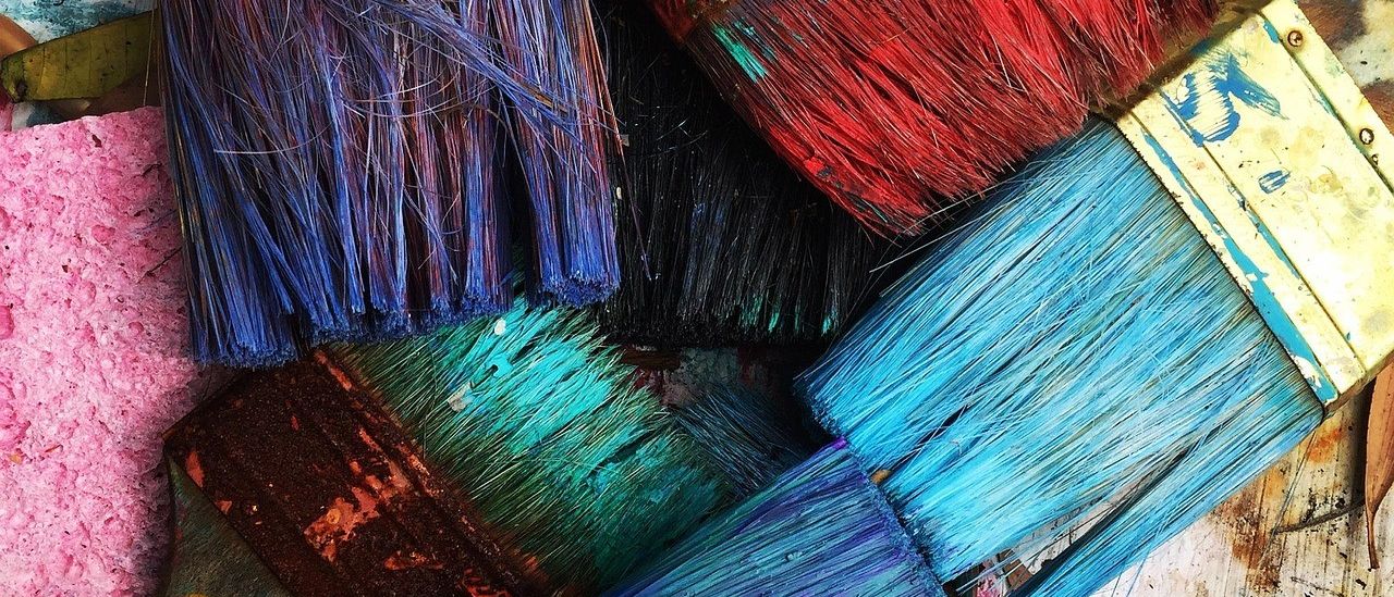 Verschiedene Pinsel, bedeckt mit verschiedenen Farben, auf einer Holzoberfläche mit Farbspritzern herum.