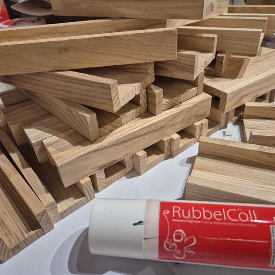Ein Nahaufnahme von mehreren Holzbrettern, die übereinander gestapelt sind. Ein Tube Rubbed Coll liegt vor den Brettern auf dem Tisch.