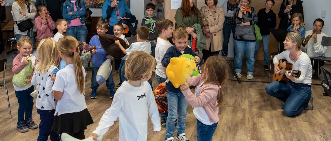 Eine Gruppe von Kindern spielt mit Kuscheltieren, während Erwachsene in der Nähe zusehen.