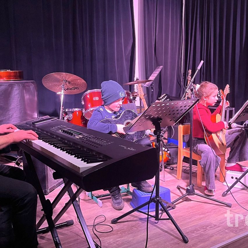Zwei Kinder spielen Gitarre auf der Bühne mit einem Klavier und Trommeln vor ihnen.