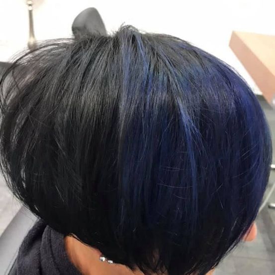 Eine Frau mit kurzen, dunklen Haaren, die an den Seiten blau gefärbt sind, sitzt in einem Salon.