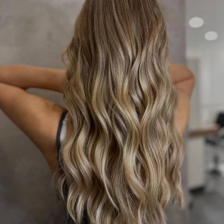 Eine Frau mit langen, welligen blonden Haaren in lockeren Wellen, die in einem Salon steht.