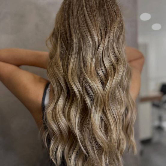 Eine Frau mit langen, welligen blonden Haaren in lockeren Wellen, die in einem Salon steht.