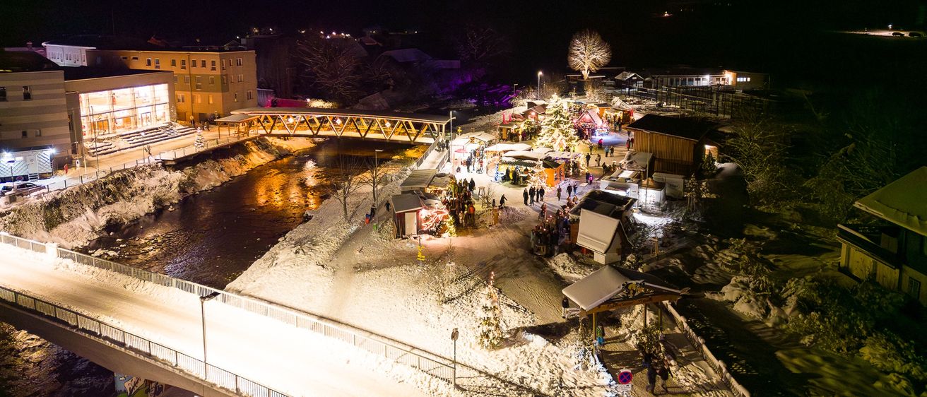 Eine Luftaufnahme einer Stadt bei Nacht mit einer Brücke über einem Fluss und vielen Menschen rund um Stände.