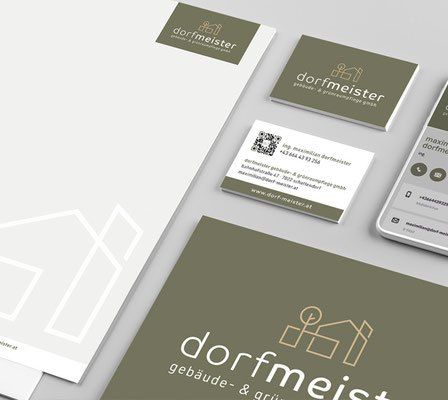 Ein Set an Branding-Materialien umfasst Visitenkarten, einen Ordner, ein Handy und Büroklammern. Die Karten zeigen ein Logo eines Hauses und den Namen Dorfmeister. Das Handy zeigt den Text Dorfmeister und einen QR-Code an.