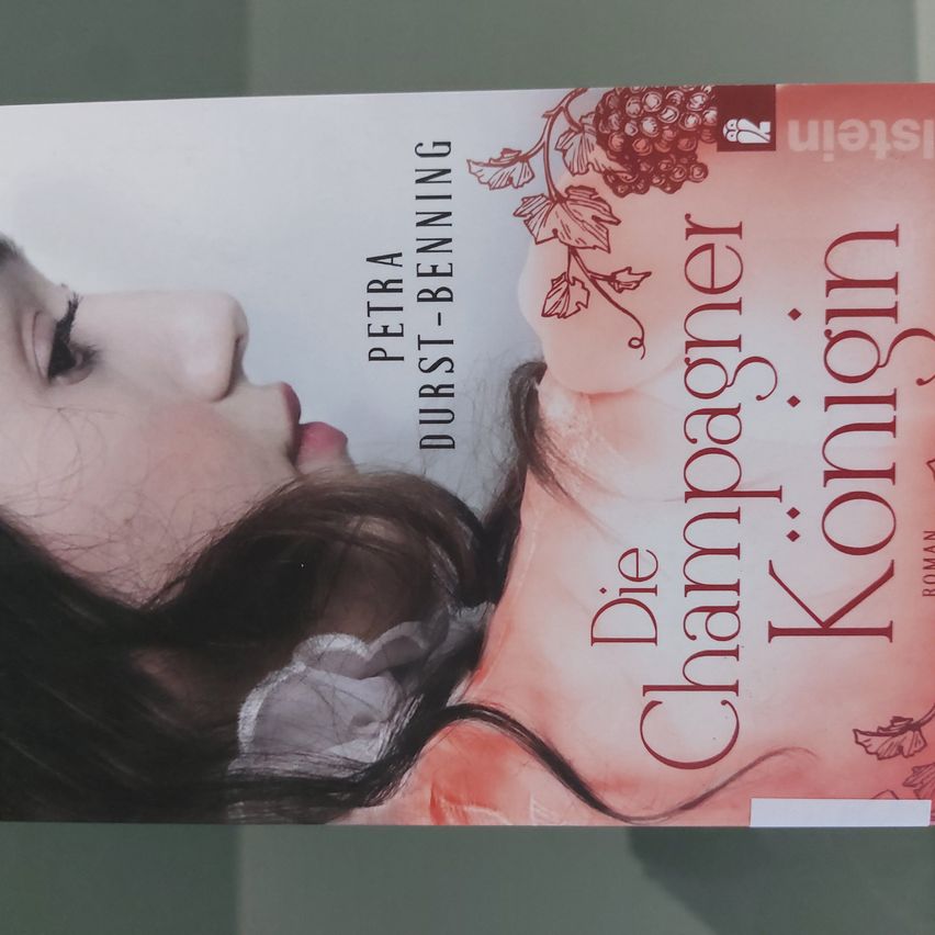 Buchcover mit dem Gesicht einer Frau mit langen dunklen Haaren, das eine weiße Spitze auf der Schulter trägt, und einem rosa Hintergrund mit Text auf Deutsch und Englisch.