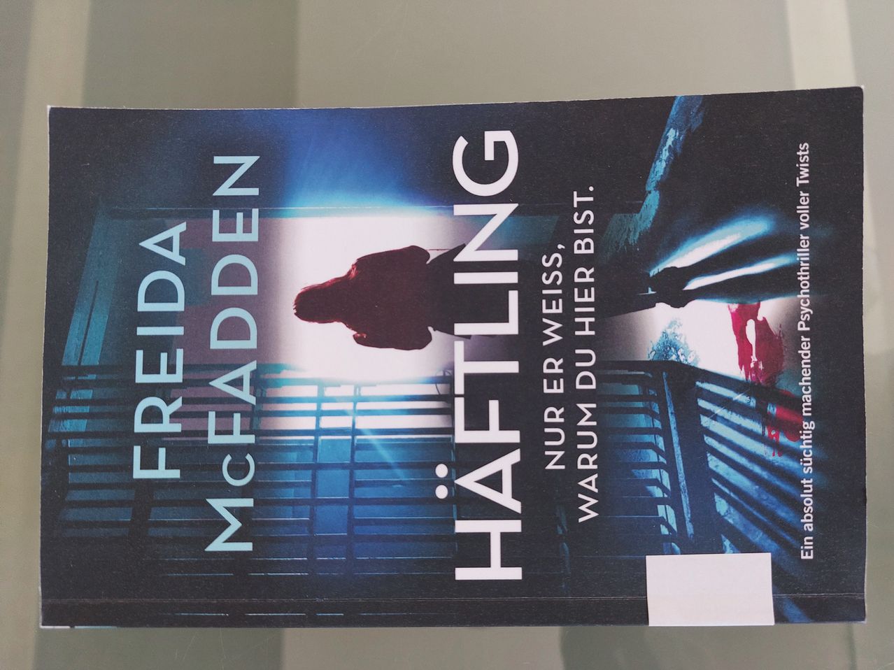 Buchcover für 'Haftling' von Freida McFadden, zeigt eine Silhouette einer Person in einem dunklen Raum mit Licht, das durch ein Fenster scheint.