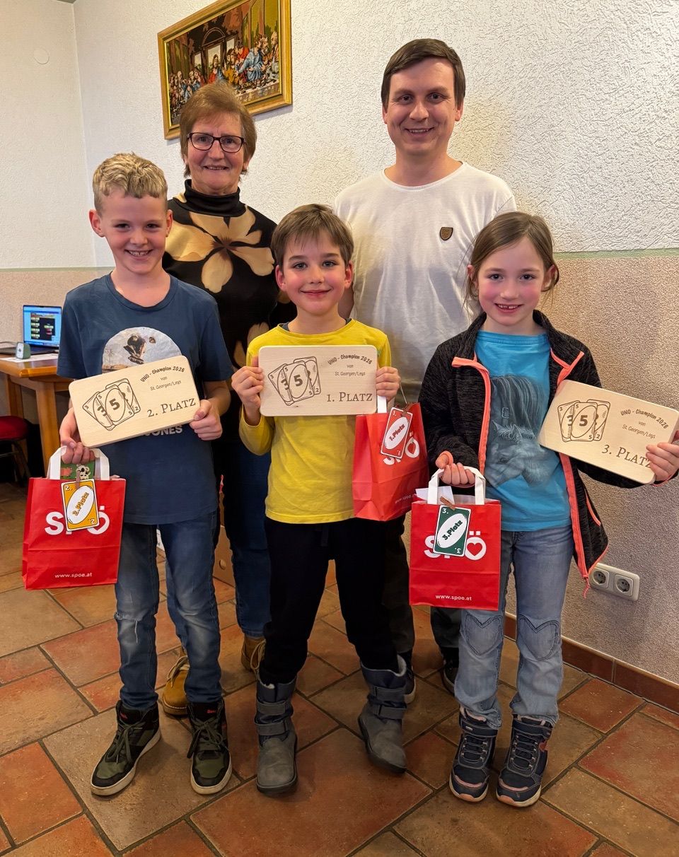 Eine Familie posiert für ein Foto mit vier Kindern, die Urkunden und Tüten halten, einer Frau mit Brille und einem Mann in einem weißen T-Shirt.