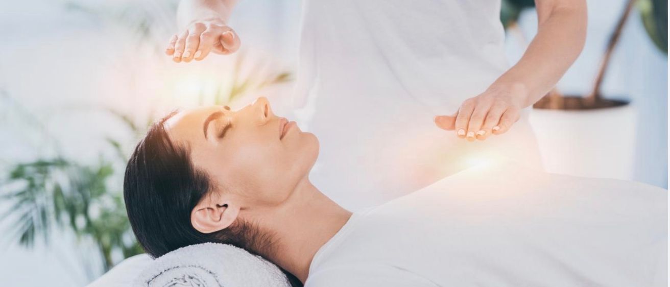 Eine Frau liegt auf einem Massagetisch und erhält eine Lichttherapiebehandlung von einem Therapeuten in einem weißen Gewand. Die Hände des Therapeuten strahlen ein warmes Leuchten aus.