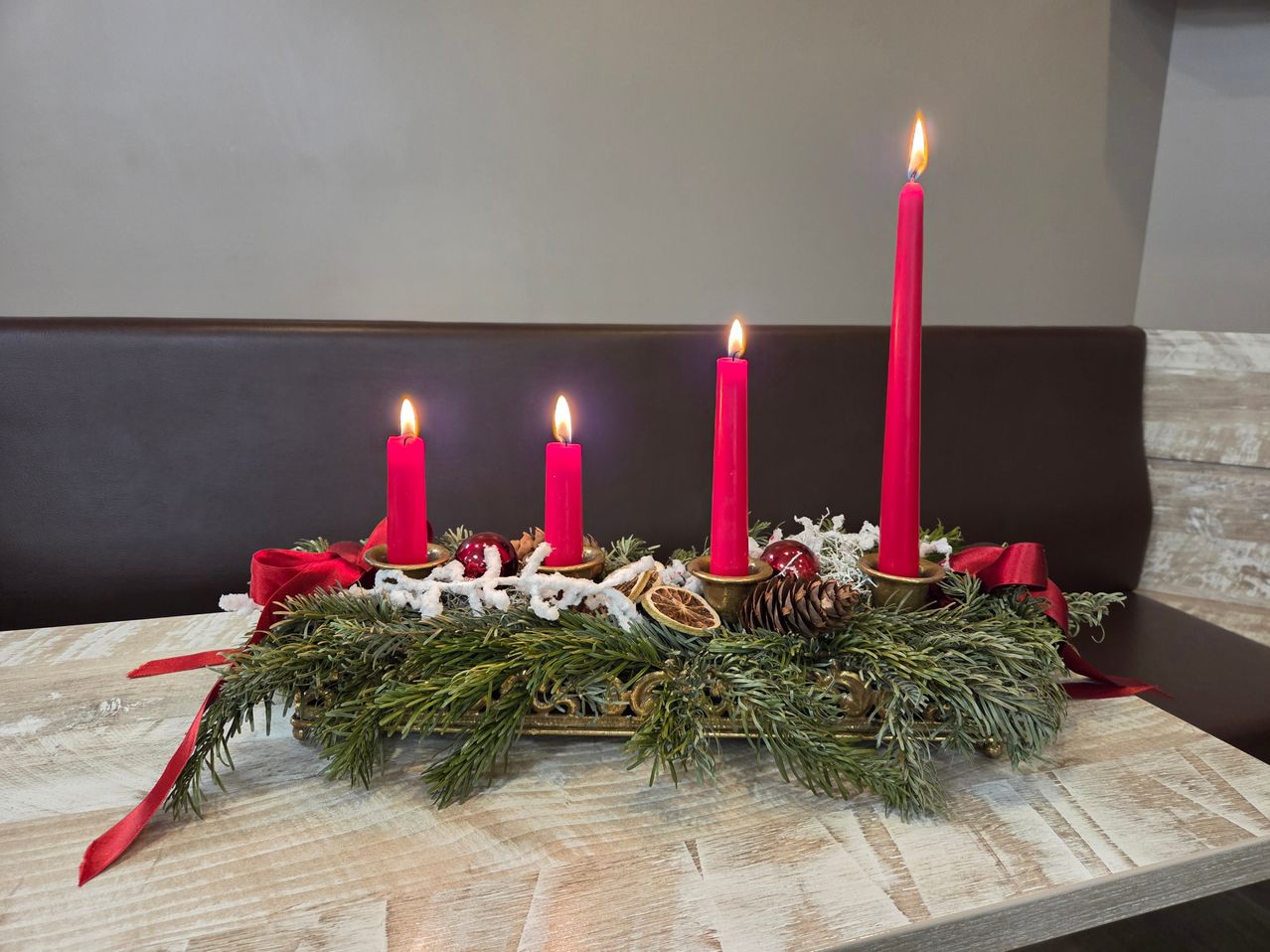 Ein goldener Kerzenständer mit vier roten Kerzen und Weihnachtsdekorationen steht auf einem Holztisch.