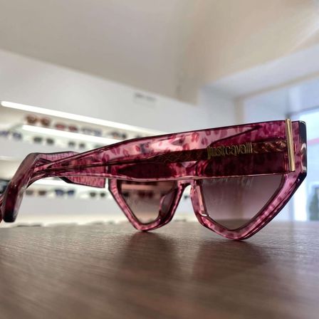 Ein Paar pinke Just Cavalli Sonnenbrille mit Leopardenmuster-Rahmen liegt auf einem Holztisch in einem Geschäft.