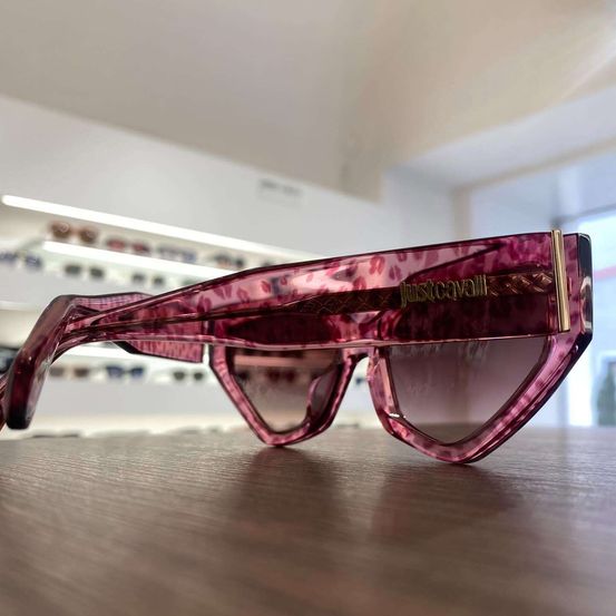 Ein Paar pinke Just Cavalli Sonnenbrille mit Leopardenmuster-Rahmen liegt auf einem Holztisch in einem Geschäft.
