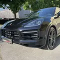 Ein schwarzer Porsche Cayenne ist vor einem Gebäude mit einem Baum und einer Straßenlaterne im Hintergrund geparkt.