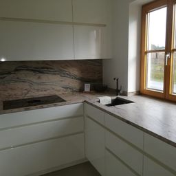 Eine moderne Küche mit weißen Schränken, Marmorarbeitsplatten, einem Waschbecken und einem Herd, mit einem Fenster, das einen Blick auf ein Grasfeld bietet.