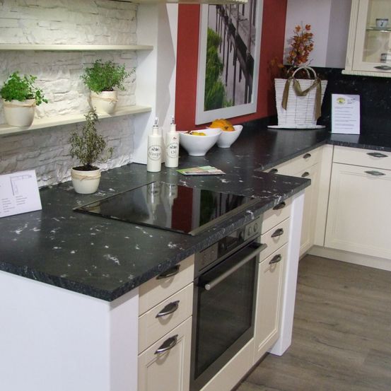 Eine moderne Küche mit schwarzem Marmorarbeitsplatten, einem schwarzen Herd und weißen Schränken. Es gibt Topfpflanzen auf den Regalen und einen Korb auf der Arbeitsplatte. Die Küche hat eine rote Wand mit einem Bilderrahmen.