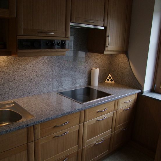 Eine Küche mit Granitarbeitsplatten, Holzschränken und einem Herd auf der Arbeitsplatte. Eine Rolle Papiertücher und ein dreieckiges Objekt befinden sich ebenfalls auf der Arbeitsplatte.