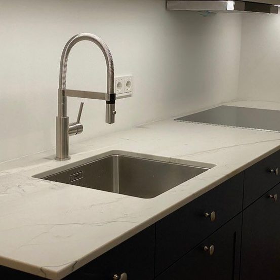 Eine moderne Küche mit Marmorarbeitsplatte, Edelstahlspüle, Chromhahn und Kochplatte. Weiße Wände und schwarze Schränke vervollständigen das minimalistische Design.