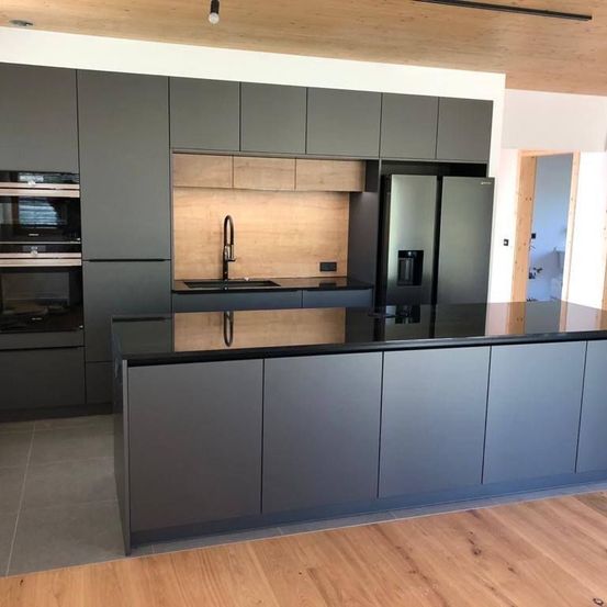 Eine moderne Küche mit dunklen Schränken, einer schwarzen Arbeitsplatte, einem doppelten Edelstahlkühlschrank, einer Holzwand und einer Deckenlampe.