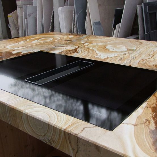 Ein modernes schwarzes Induktionskochfeld liegt auf einem Holzarbeitsplatten mit Marmormuster. Das Kochfeld ist schlank und reflektierend und zeigt eine verschwommene Reflexion.