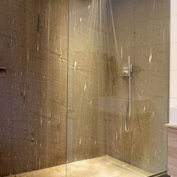 Ein moderner Duschbereich mit einer Glaswand und gefliestem Boden, Wasser fließt aus einem Duschkopf.